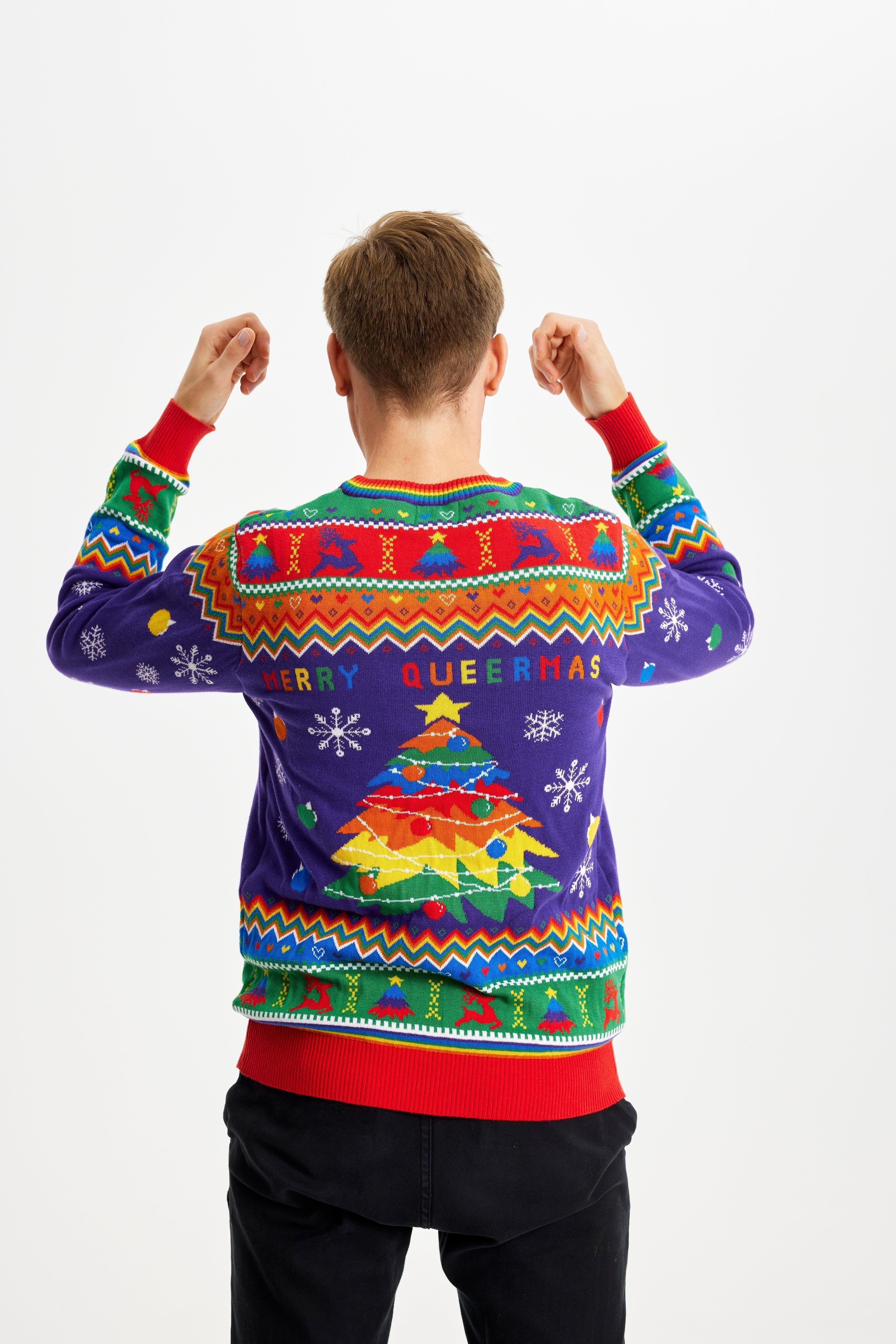 Homme posant le dos tourné et portant un pull de Noël aux couleurs de l'arc-en-ciel avec la citation